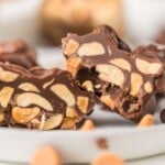 Close-up of chocolate nut clusters with visible peanuts inside, displayed on a white plate.