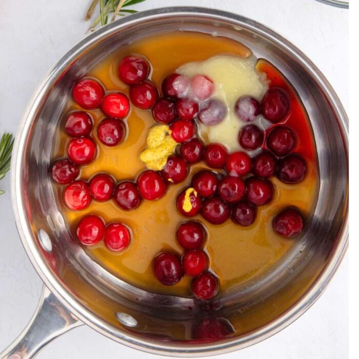 Cranberries, honey, Dijon mustard, and butter in a saucepan, ready to be cooked.