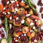 Roasted Brussels sprouts, carrots, pecans, goat cheese, cranberries, and rosemary arranged on a white platter.