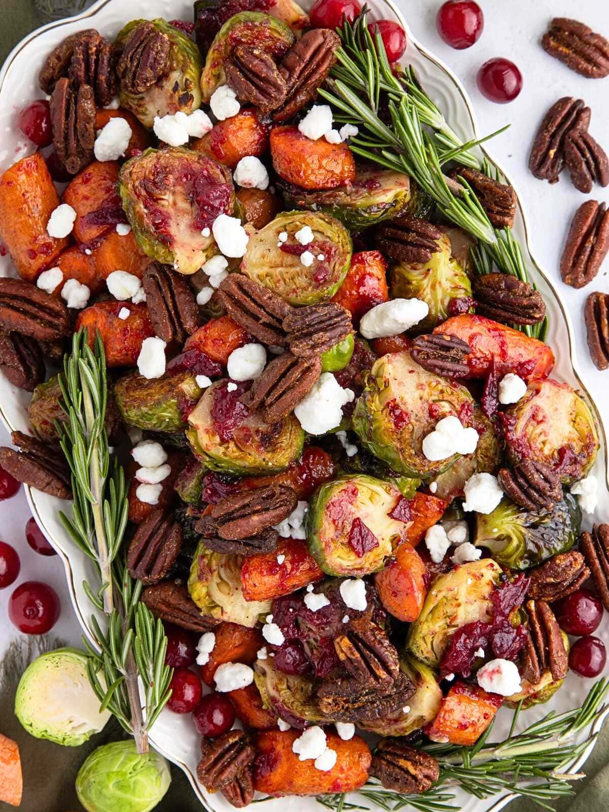 Roasted Brussels sprouts, carrots, pecans, goat cheese, cranberries, and rosemary arranged on a white platter.