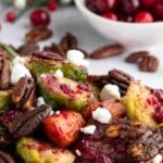 Roasted Brussels sprouts with pecans, goat cheese, and cranberries, with fresh cranberries in the background.