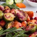 Roasted Brussels sprouts and carrots with fresh rosemary and cranberries on a plate.