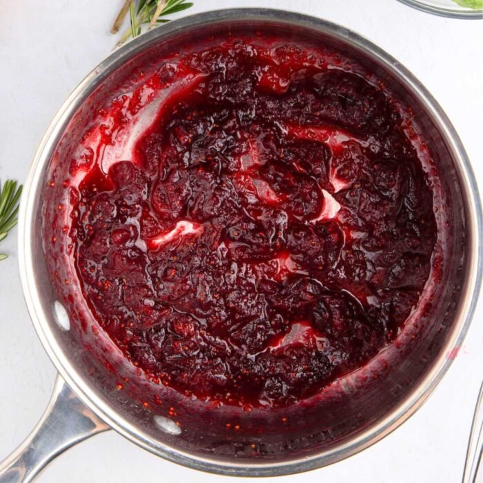 A saucepan filled with thick, homemade cranberry sauce on a white surface.