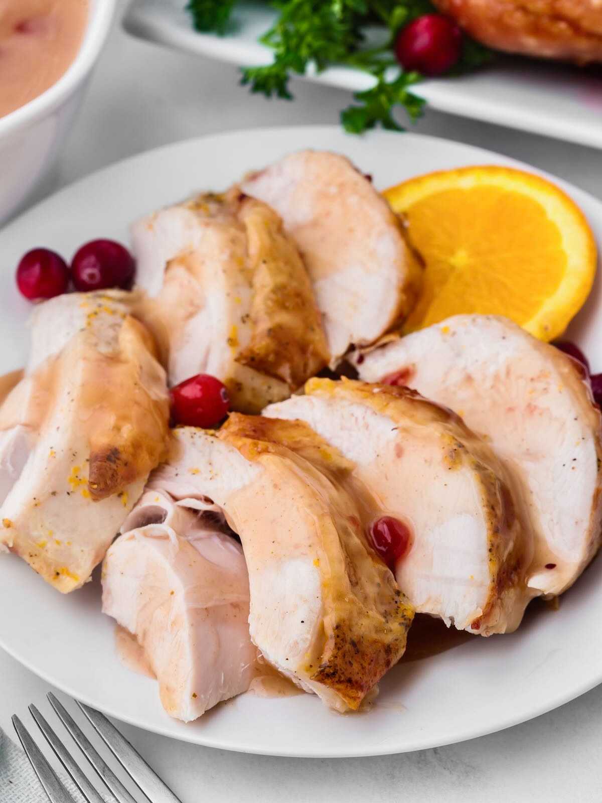 Sliced roasted turkey breast with cranberries and an orange slice on a white plate.