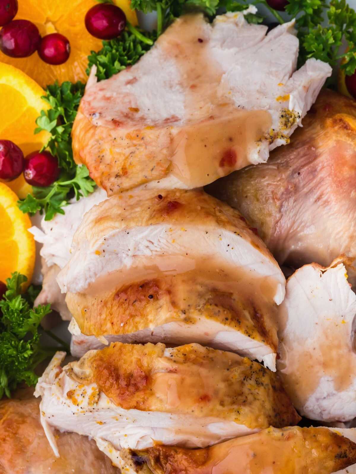 Sliced roasted turkey breast with orange slices, cranberries, and parsley garnish.