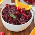 A bowl of whole berry cranberry sauce garnished with orange slices and cranberries, on a wooden board.
