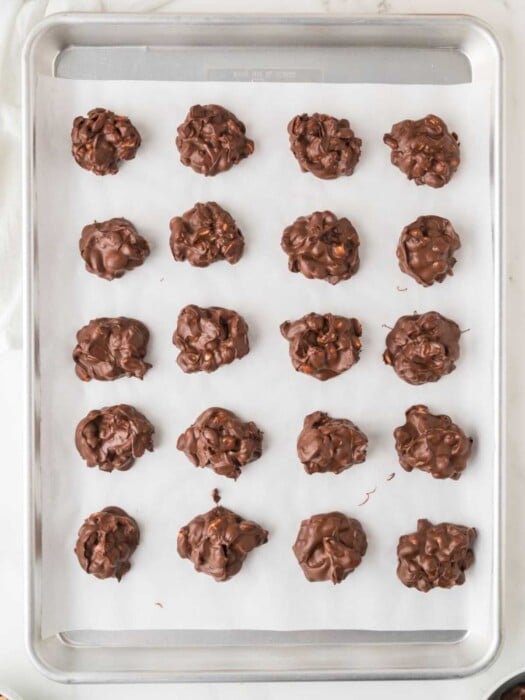 Clusters of chocolate-covered nuts are arranged in neat rows on a parchment-lined baking sheet.