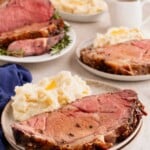 A plate with prime rib and mashed potatoes, with more servings and gravy in the background.