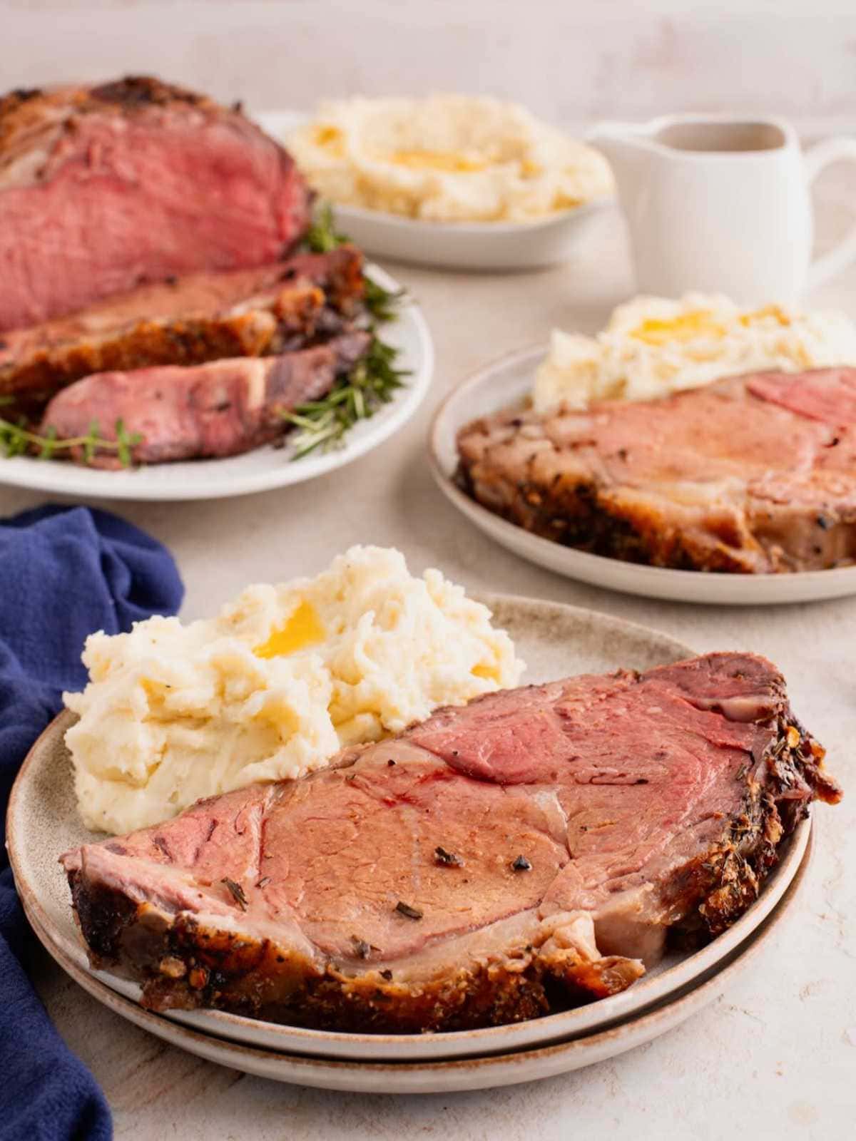 A plate with prime rib and mashed potatoes, with more servings and gravy in the background.