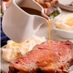 Gravy being poured over a thick slice of prime rib with mashed potatoes on the side.