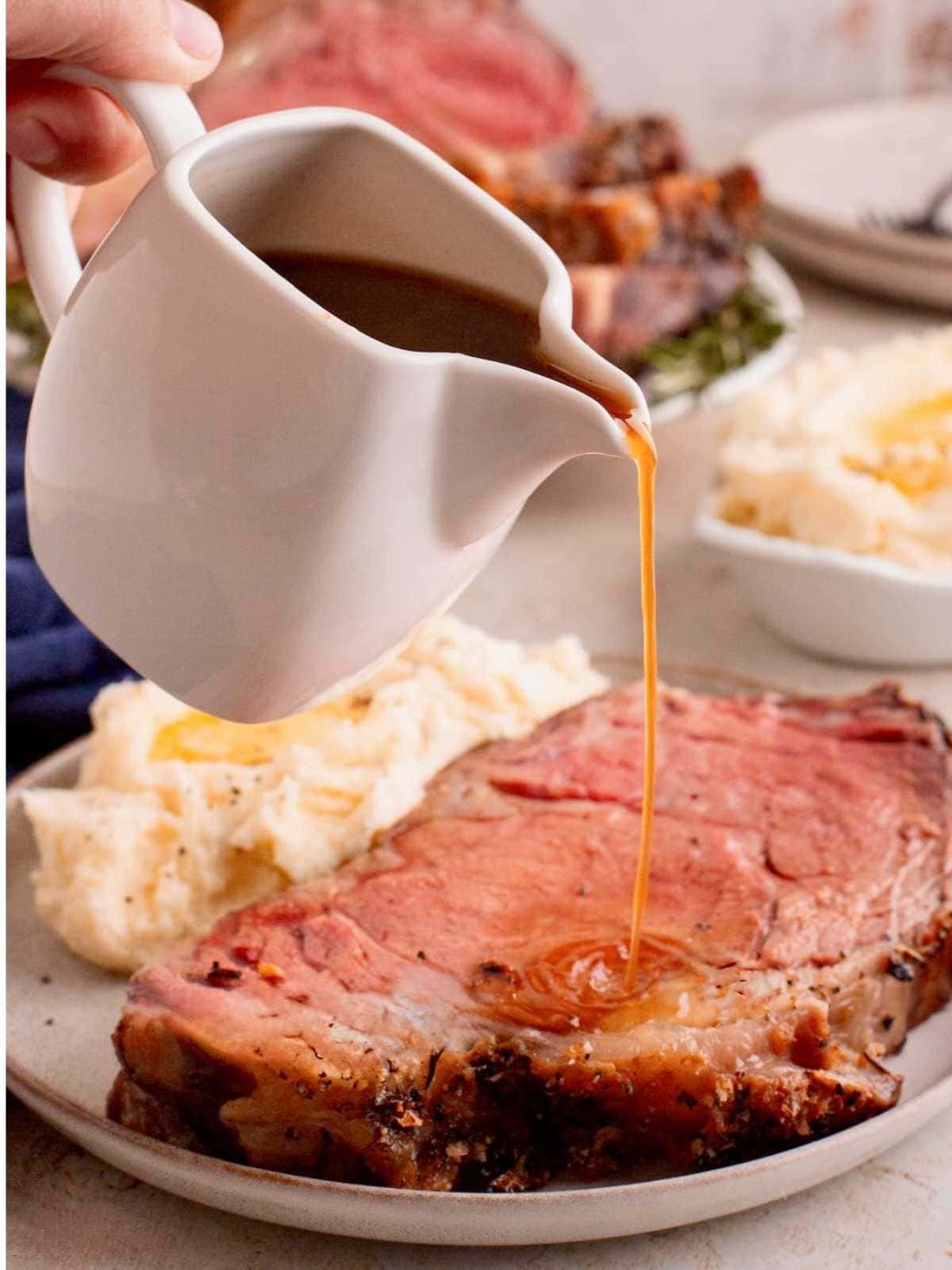 Gravy being poured over a thick slice of prime rib with mashed potatoes on the side.