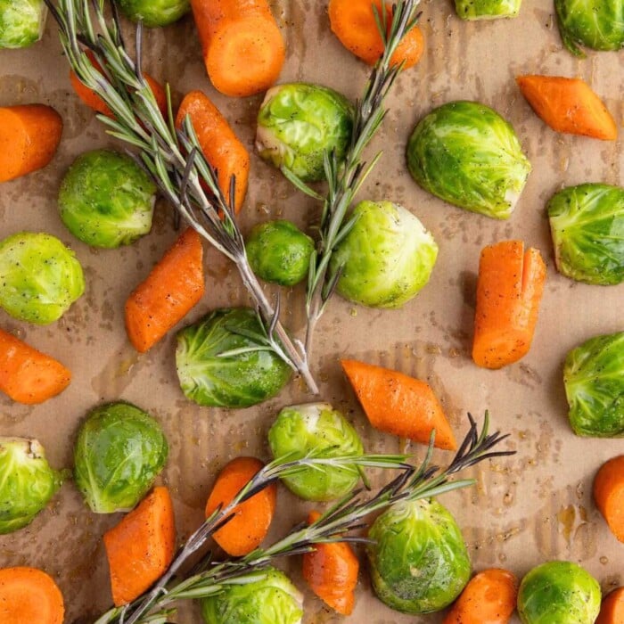 Chopped carrots, Brussels sprouts, and rosemary sprigs on a parchment-lined baking sheet.