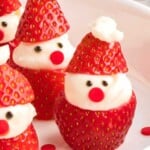 Strawberries decorated as Santa Claus with cream and chocolate details on a white plate.