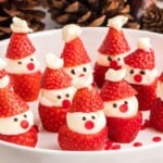 Strawberries decorated as mini Santa faces with cream and chocolate, displayed on a white plate.