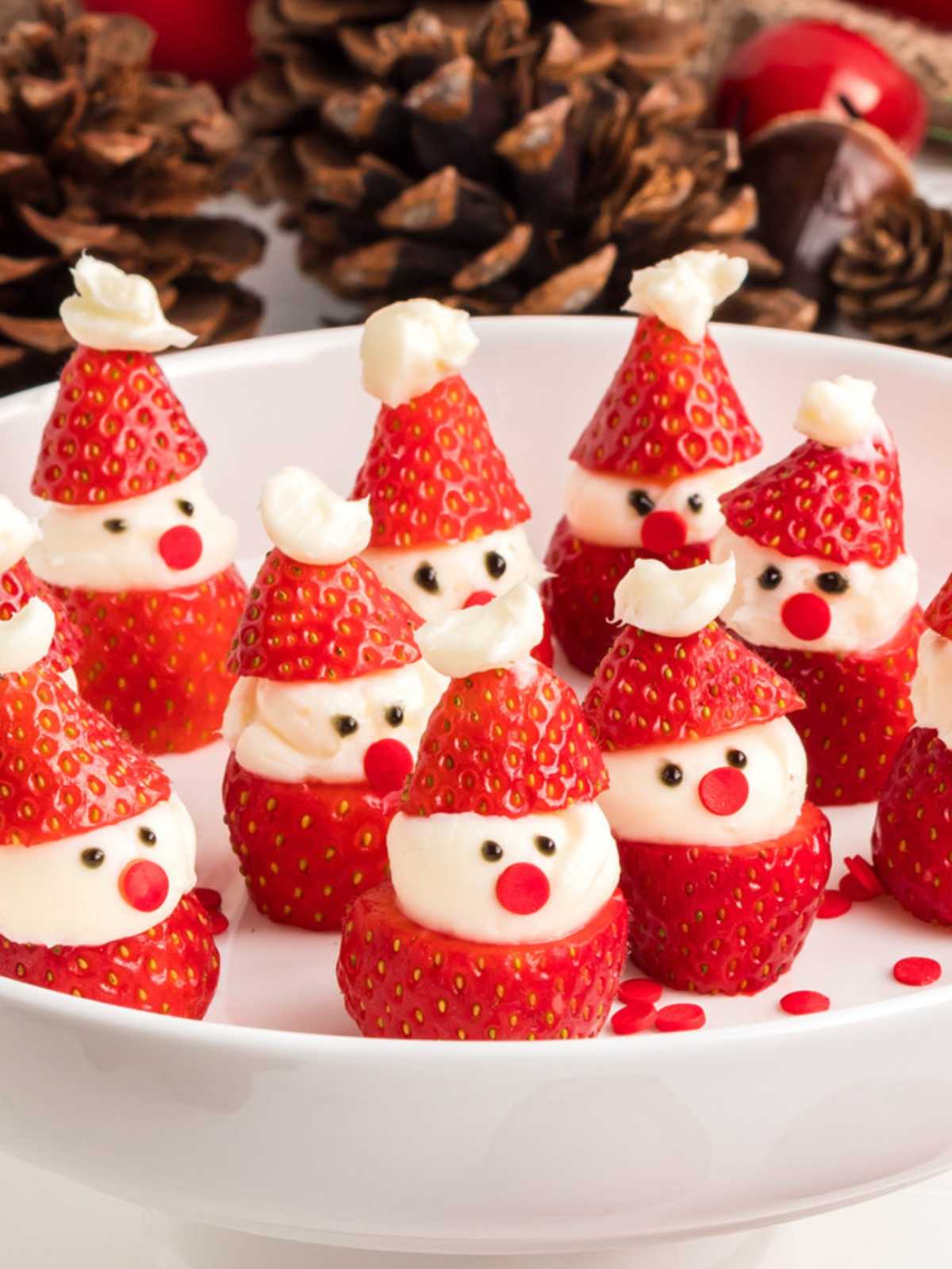 Strawberries decorated as mini Santa faces with cream and chocolate, displayed on a white plate.