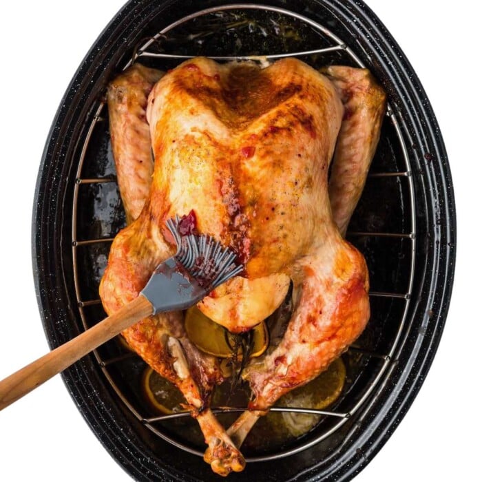 A roasted turkey in a pan being brushed with glaze or juices using a basting brush.
