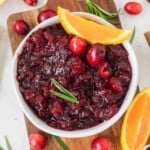 A bowl of cranberry sauce garnished with fresh cranberries, orange slices, and a sprig of rosemary.