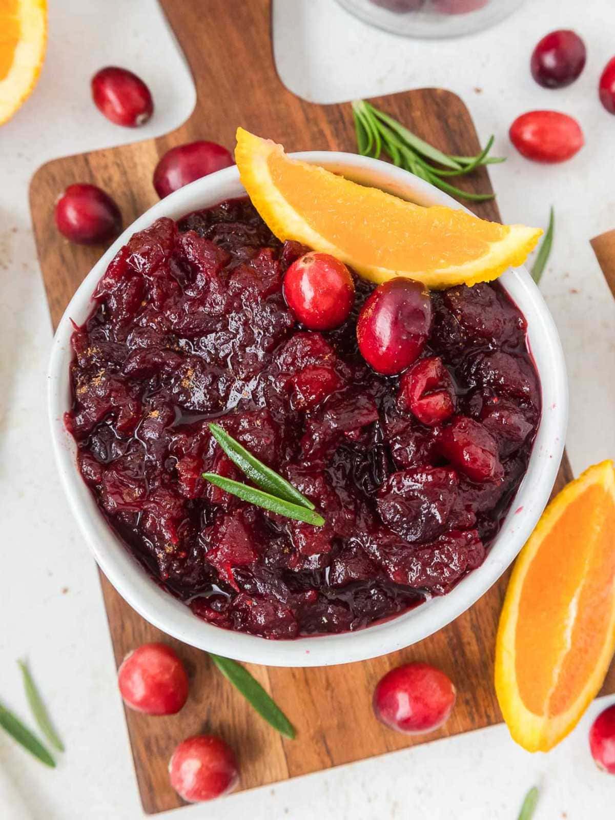 A bowl of cranberry sauce garnished with fresh cranberries, orange slices, and a sprig of rosemary.
