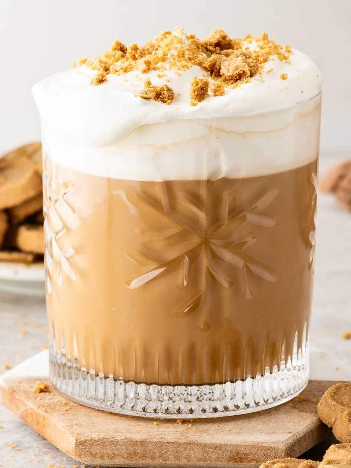 Hot coffee in a glass, topped with whipped cream and cookie crumbles.