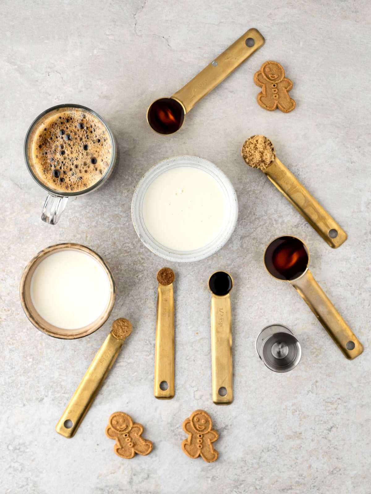 Ingredients of coffee, milk, cream, spices, brown sugar, vanilla, and gingerbread cookies on a light surface.