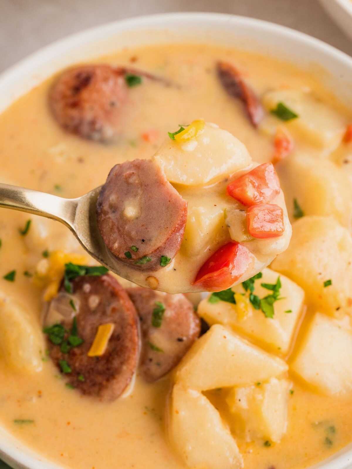 A spoonful of creamy sausage and potato soup with chunks of sausage, potatoes, and red peppers.