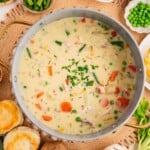 A pot of creamy chicken soup with vegetables, surrounded by biscuits, potatoes, and fresh ingredients.