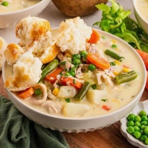 Bowl of creamy chicken pot pie soup topped with biscuit pieces, with peas and celery on the side.