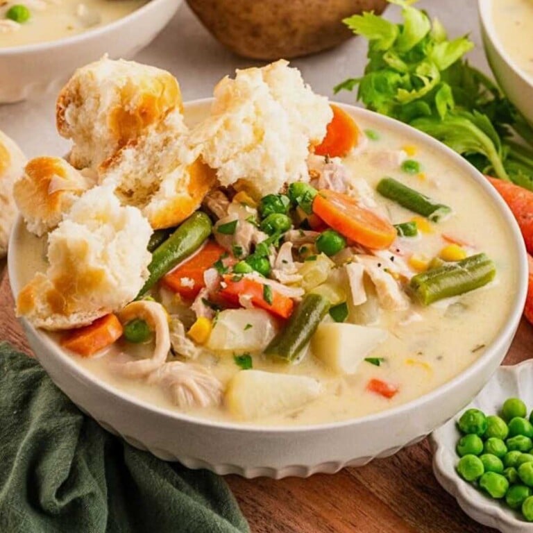 Bowl of creamy chicken pot pie soup topped with biscuit pieces, with peas and celery on the side.