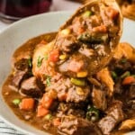 A spoonful of hearty beef stew with vegetables in a bowl on a striped cloth.