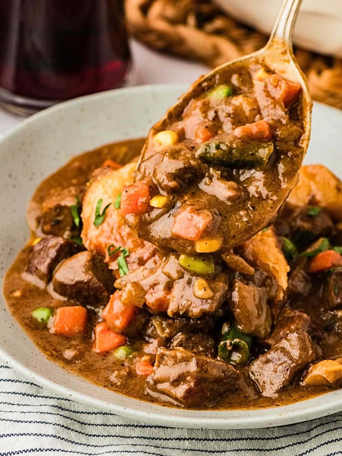 A spoonful of hearty beef stew with vegetables in a bowl on a striped cloth.