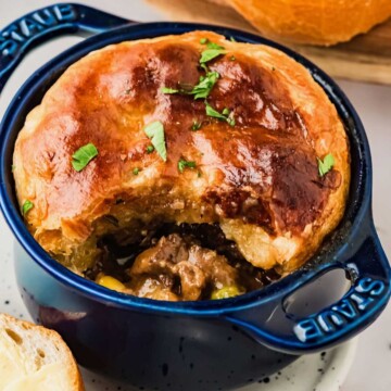 Golden, flaky beef stew pot pie with a portion eaten, revealing savory meat and vegetables inside a blue ramekin.