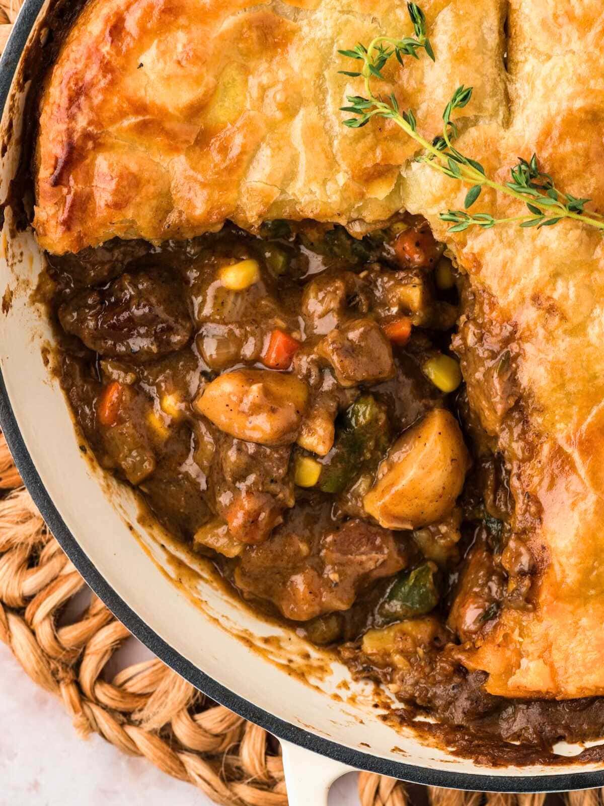 Beef pot pie with golden crust, filled with beef, potatoes, carrots, corn, and topped with fresh thyme.