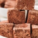 A stack of chocolate marshmallows on a white plate, dusted with cocoa powder.