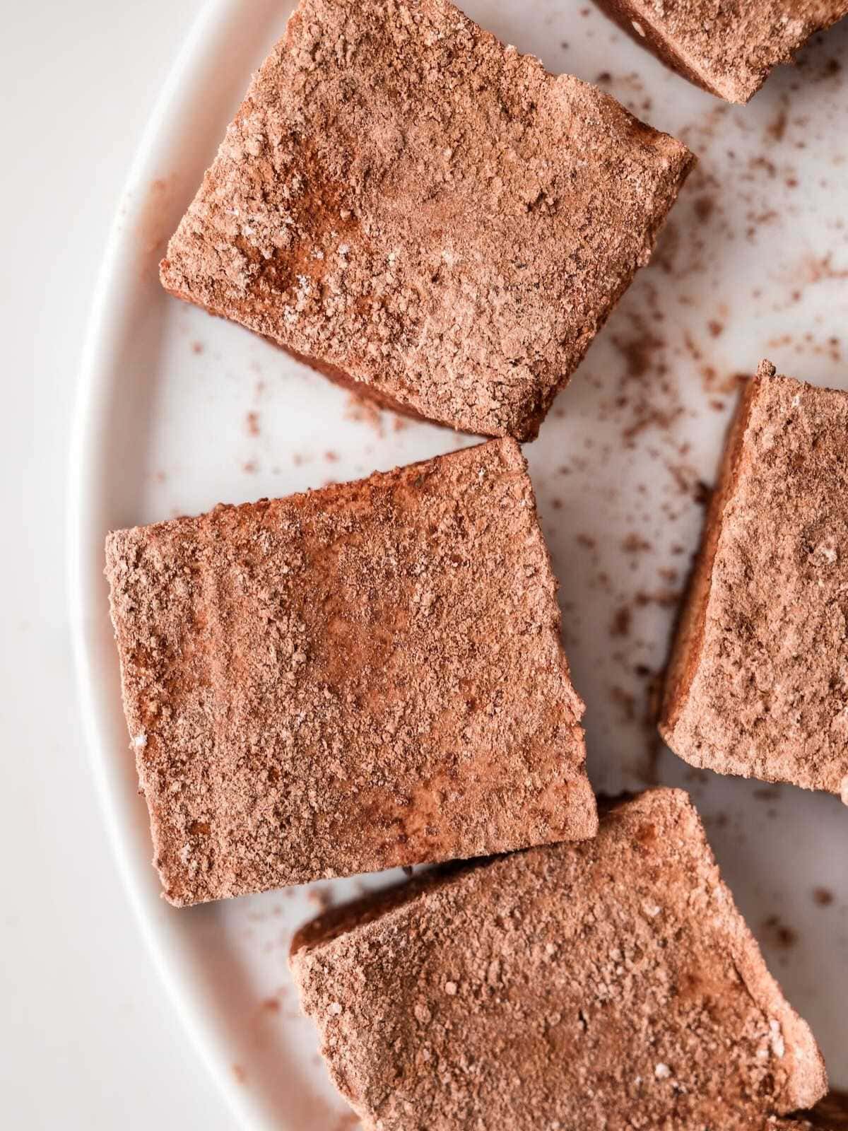 Four chocolate-dusted marshmallows on a white plate, viewed from above.