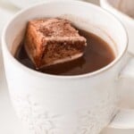 A white mug of hot chocolate with a large cocoa-dusted marshmallow floating on top.