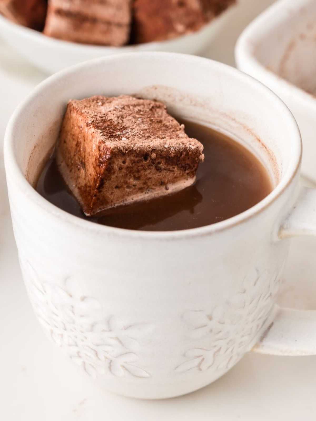 A white mug of hot chocolate with a large cocoa-dusted marshmallow floating on top.