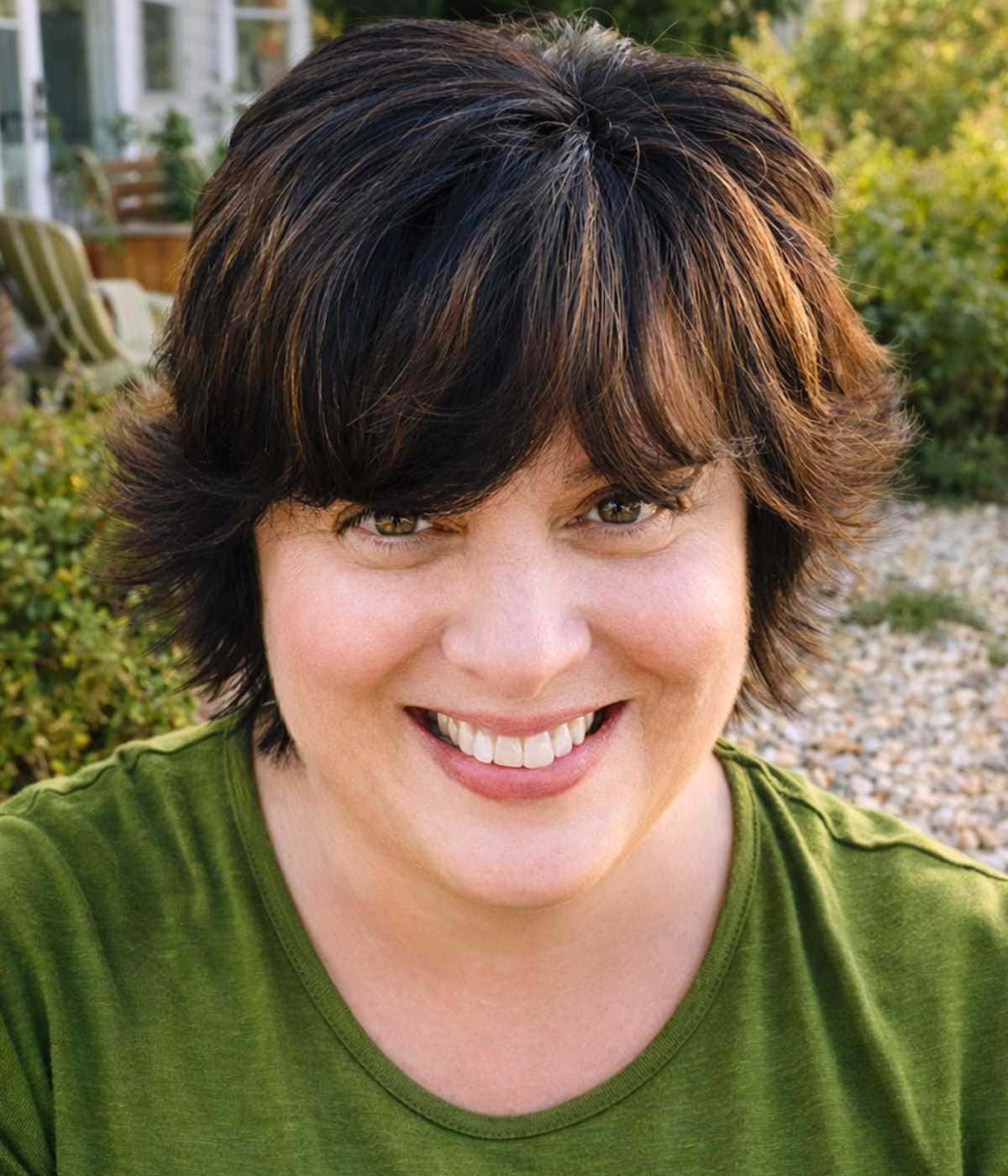 Debi Morgan in her garden smiling with a green shirt.