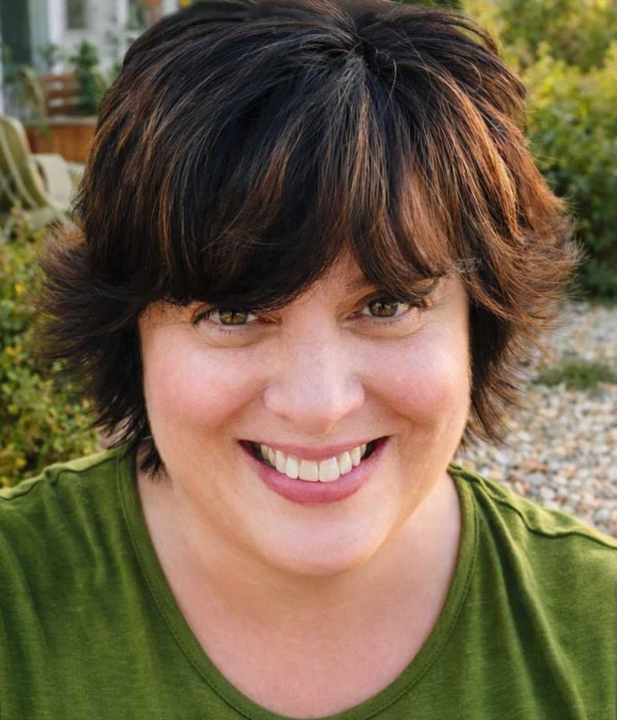 Debi Morgan with short dark hair and green shirt smiling outdoors.
