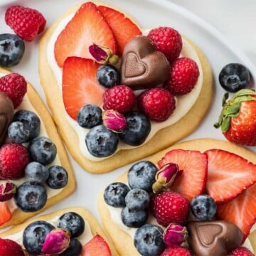 Heart shaped cookies topped with cream cheese frosting, fresh fruit and chocolate.