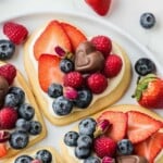 Heart-shaped cookies topped with cream, strawberries, blueberries, raspberries, and chocolate hearts on a plate.