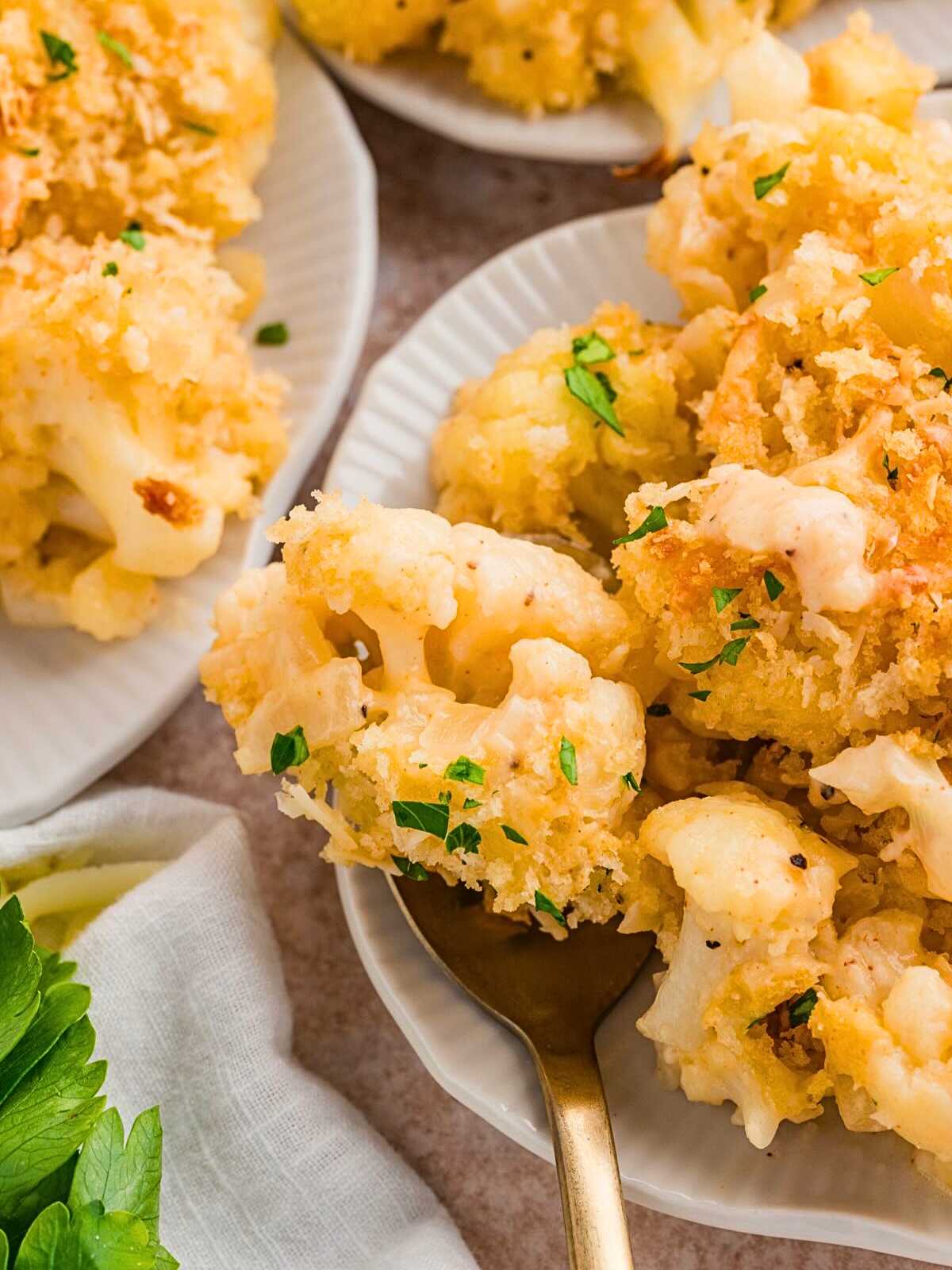 Close-up of baked cauliflower casserole with golden breadcrumbs, served on a white plate with a fork.