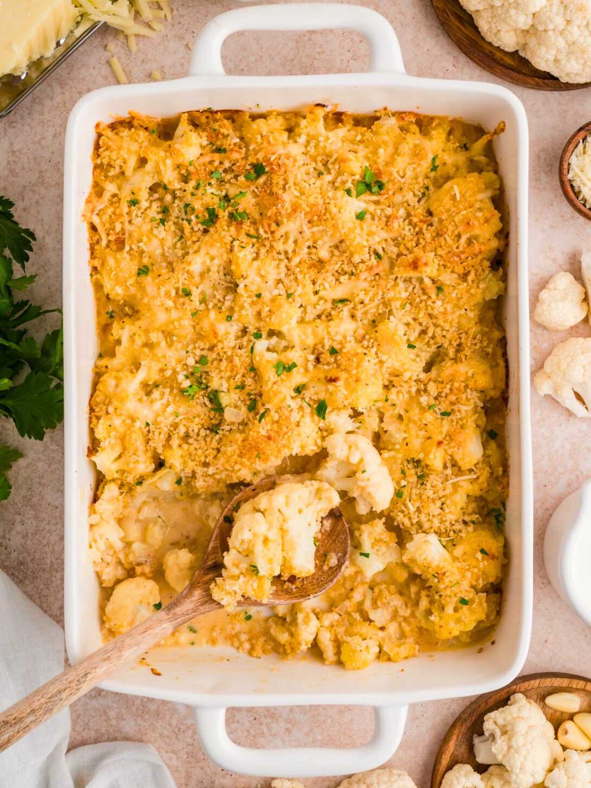 Baked cauliflower casserole with a golden breadcrumb topping, served in a white dish with a wooden spoon.