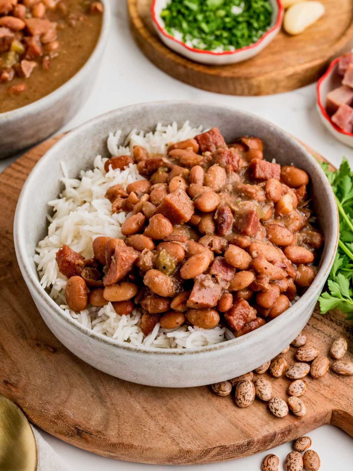 A bowl of rice topped with pinto beans and sausage, garnished with herbs, on a wooden board.