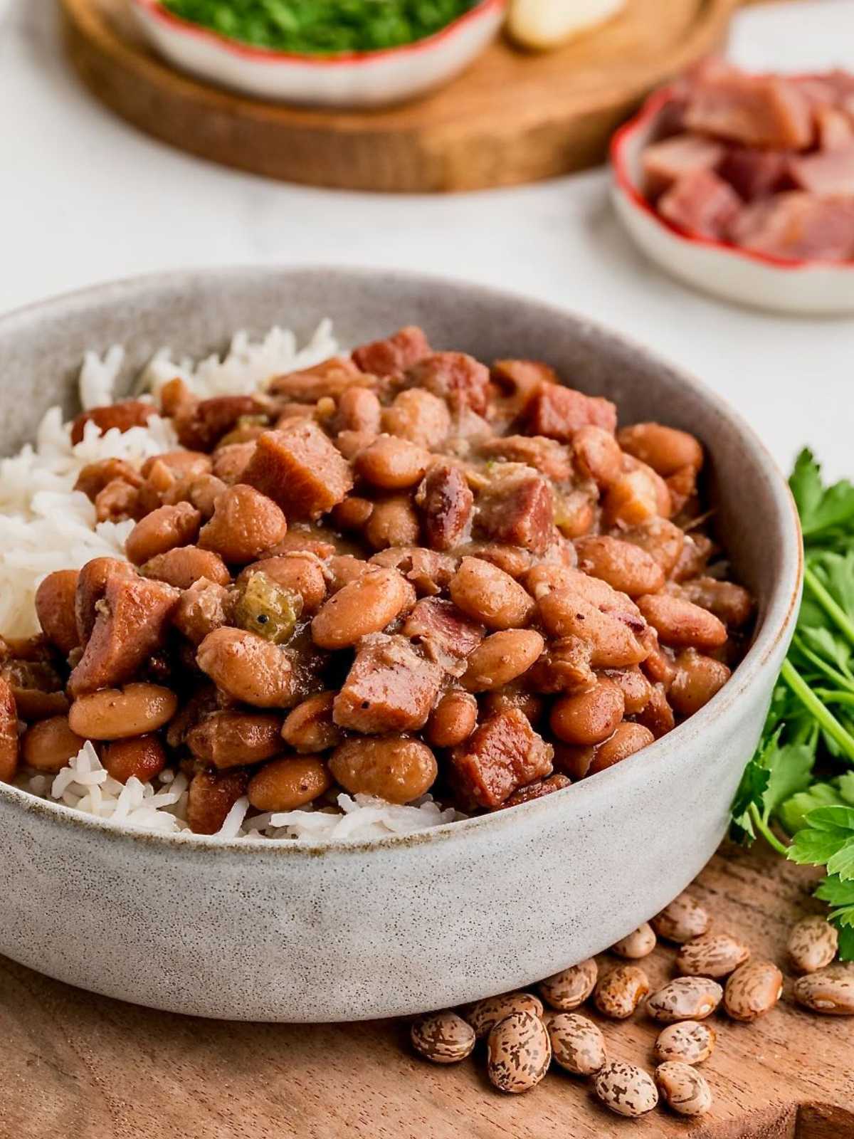 A bowl of white rice topped with stewed pinto beans and pieces of ham, garnished with fresh parsley.