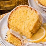 A slice of lemon cake with icing on a plate, served with lemon slices and a fork.