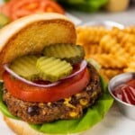 A black bean burger with lettuce, tomato, onion, pickles, and crinkle-cut fries with ketchup on the side.