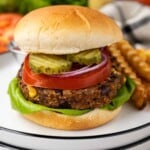 A veggie burger with lettuce, tomato, onion, and pickles on a plate with crinkle-cut fries.