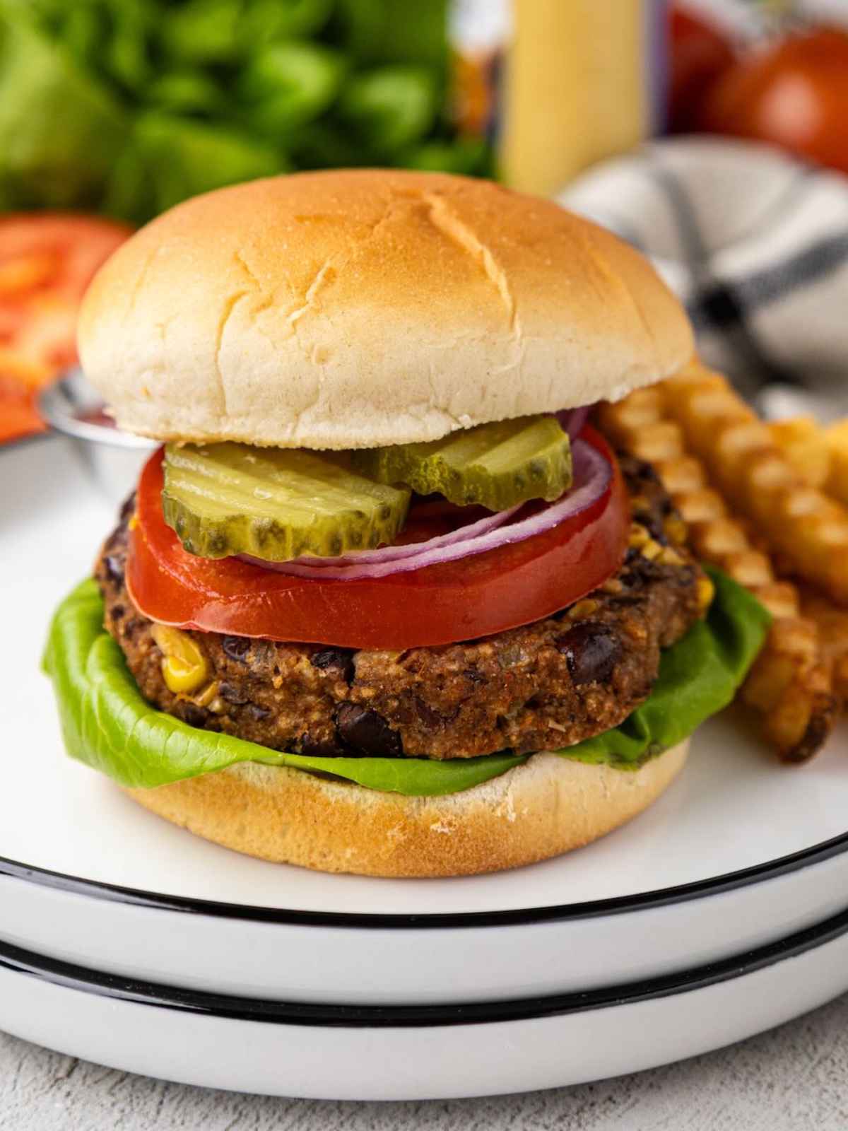 A veggie burger with lettuce, tomato, onion, and pickles on a plate with crinkle-cut fries.