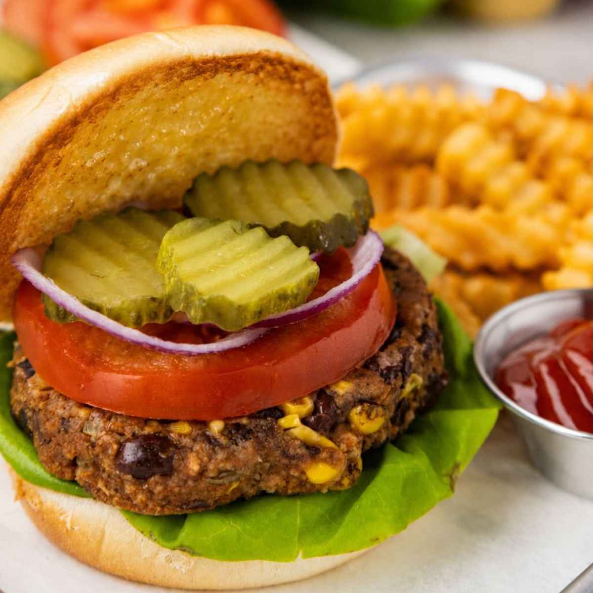 A black bean burger with lettuce, tomato, onion, pickles, and a side of crinkle fries with ketchup.