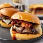 A juicy cheeseburger with bacon and barbecue sauce on a bun, served on a dark plate.
